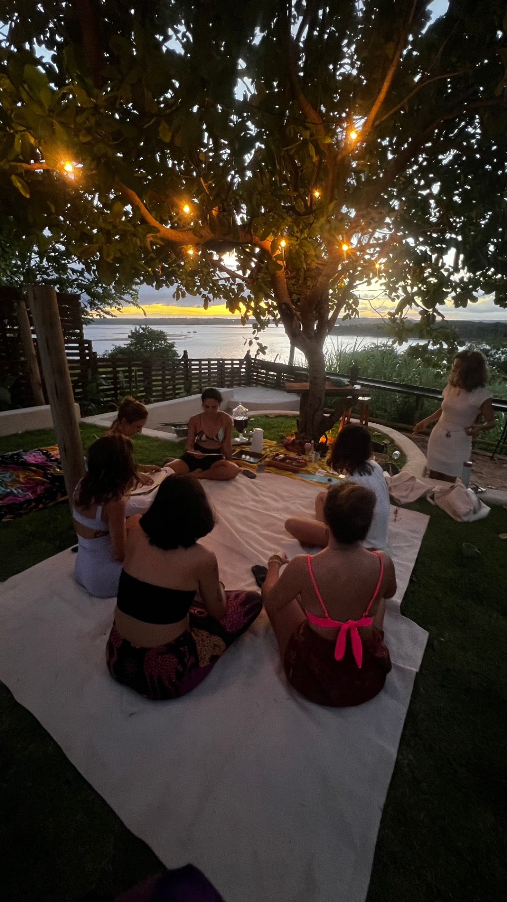 Roda de mulheres ao entardecer sob a árvore com luzes